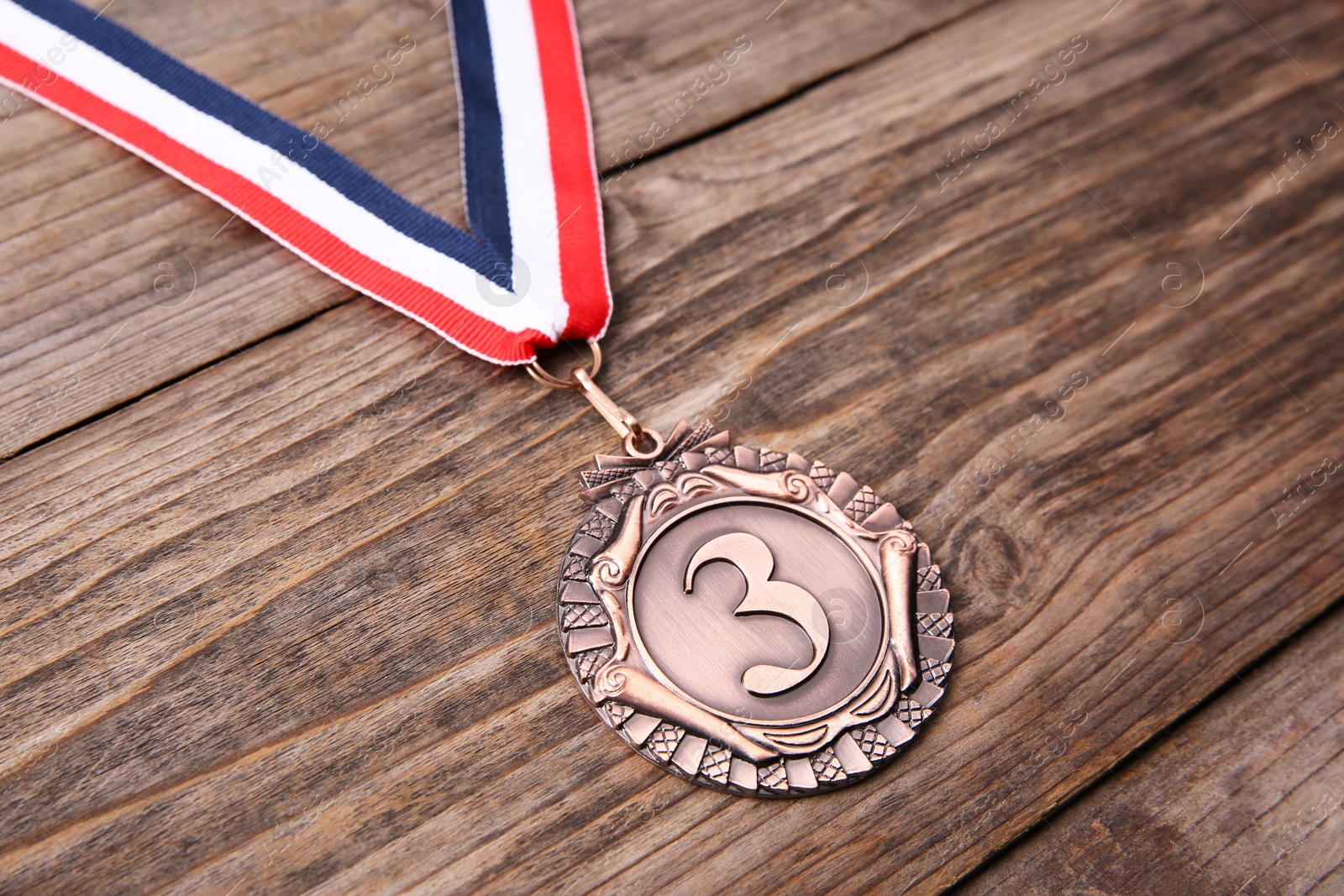 Photo of Bronze medal with striped ribbon on wooden background, closeup