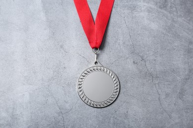 Photo of Silver medal with red ribbon on grey background, top view