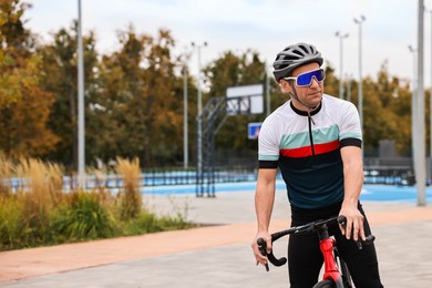 Photo of Athletic man with helmet and bicycle outdoors, space for text