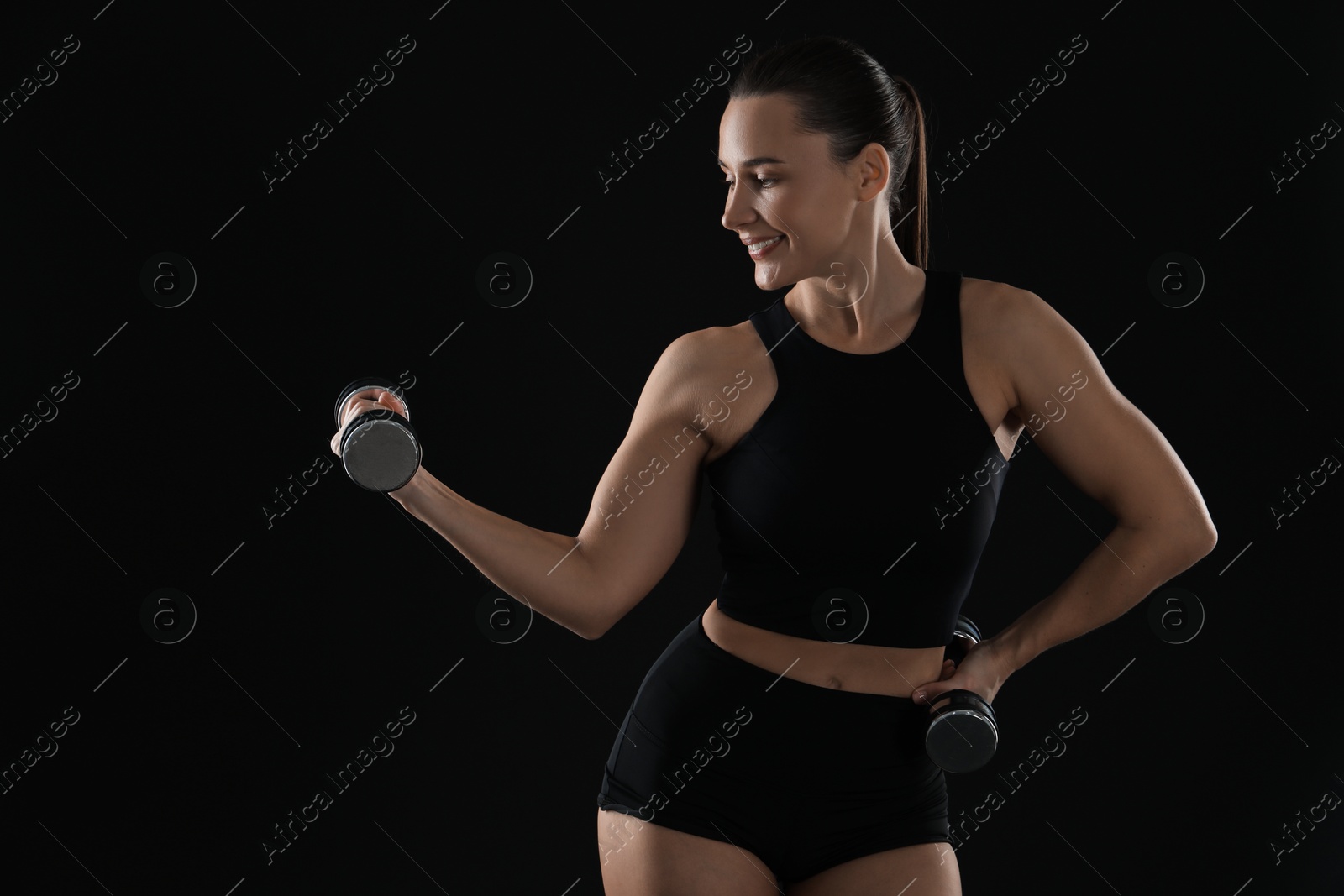 Photo of Woman exercising with dumbbells on black background