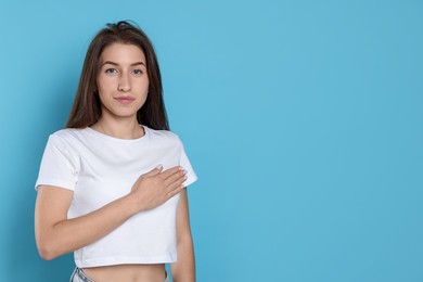 Photo of Woman making promise on light blue background, space for text. Oath gesture