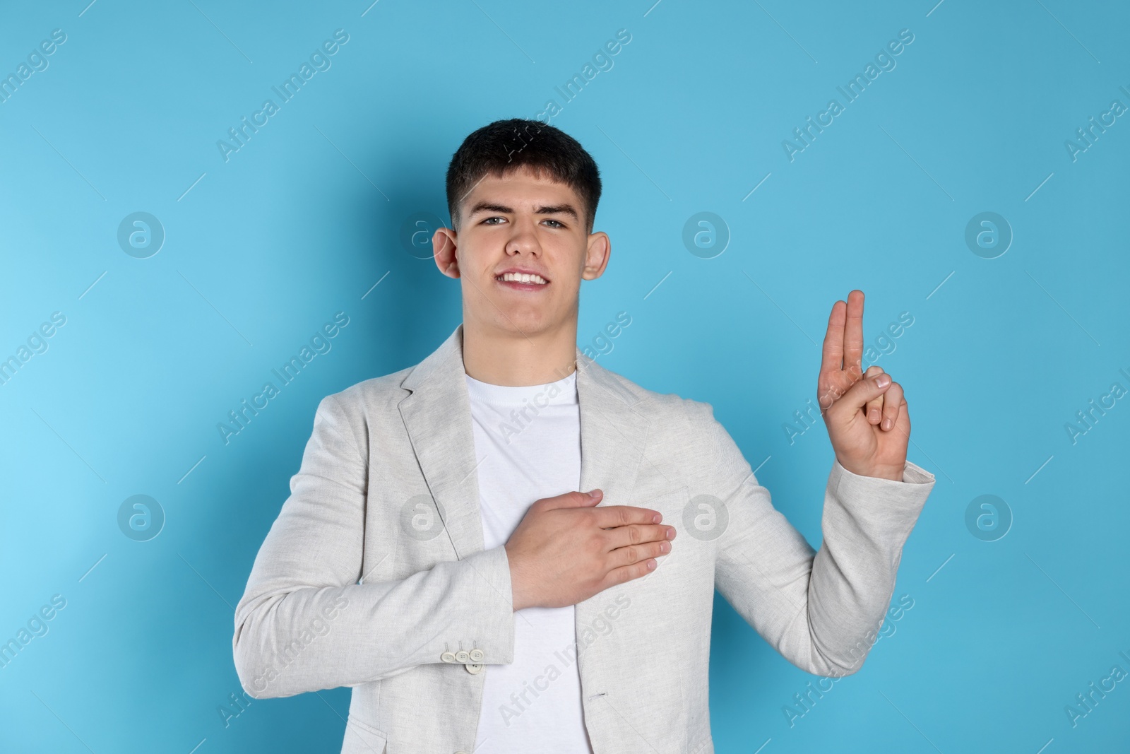 Photo of Man showing oath gesture on light blue background. Making promise