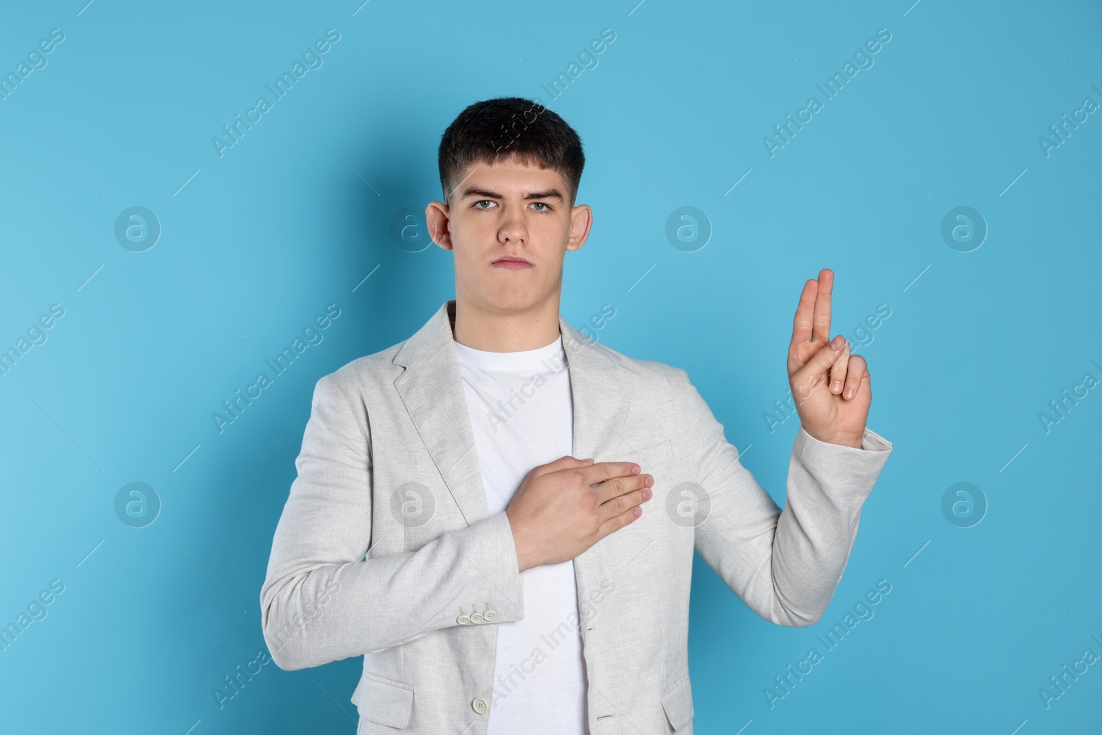 Photo of Man showing oath gesture on light blue background. Making promise