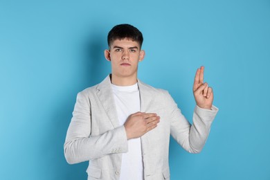 Photo of Man showing oath gesture on light blue background. Making promise