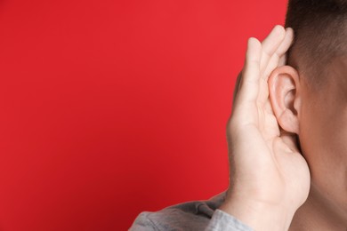 Photo of Man showing hand to ear gesture on red background, closeup. Space for text