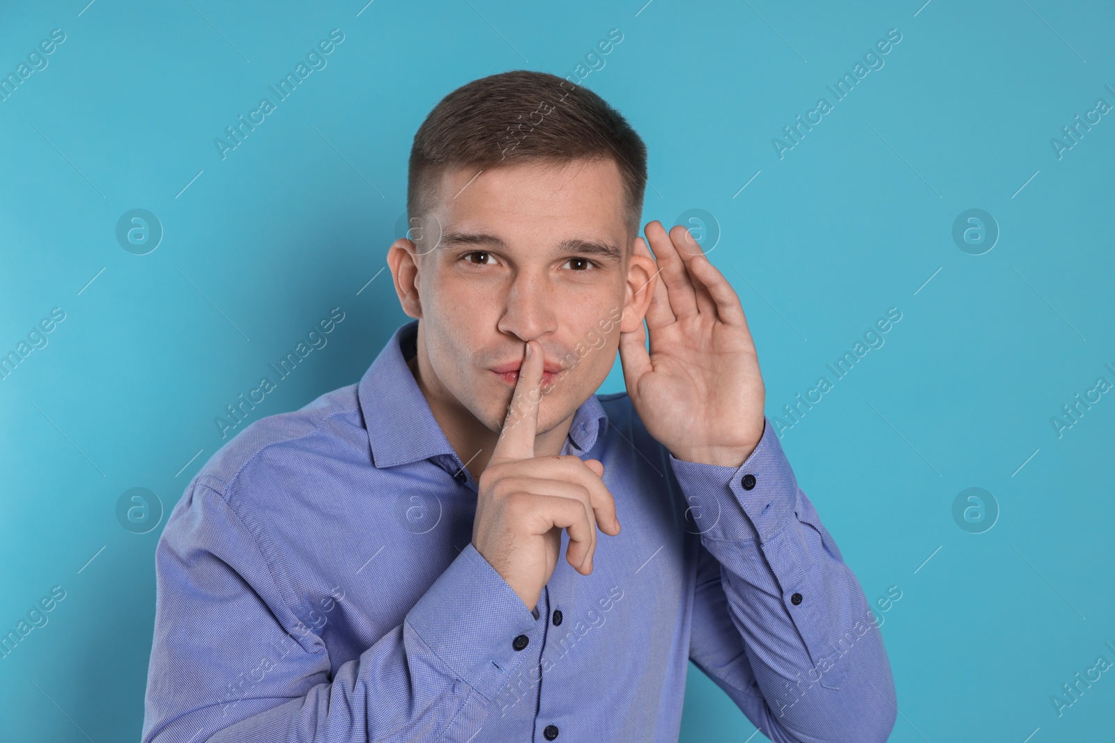 Photo of Man showing hand to ear gesture on light blue background