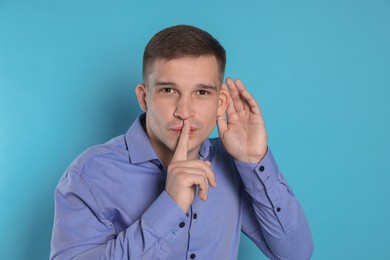 Photo of Man showing hand to ear gesture on light blue background