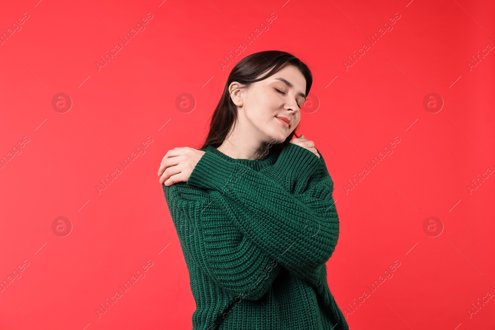 Photo of Beautiful young woman hugging herself on red background