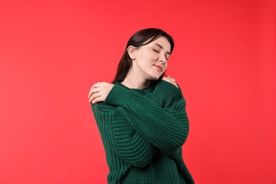 Photo of Beautiful young woman hugging herself on red background