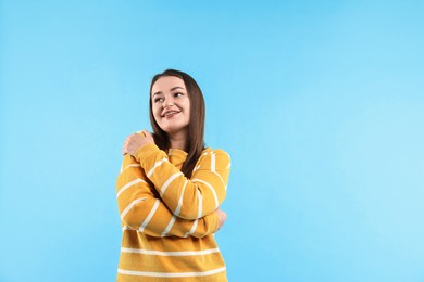 Beautiful young woman hugging herself on light blue background, space for text