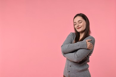 Beautiful young woman hugging herself on pink background, space for text