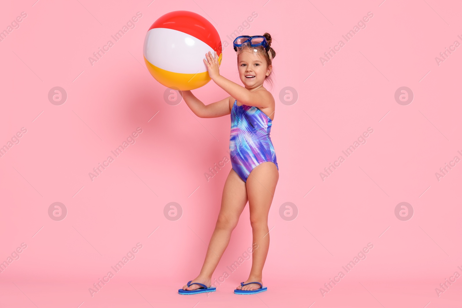 Photo of Cute little girl in swimsuit with inflatable ball on light pink background