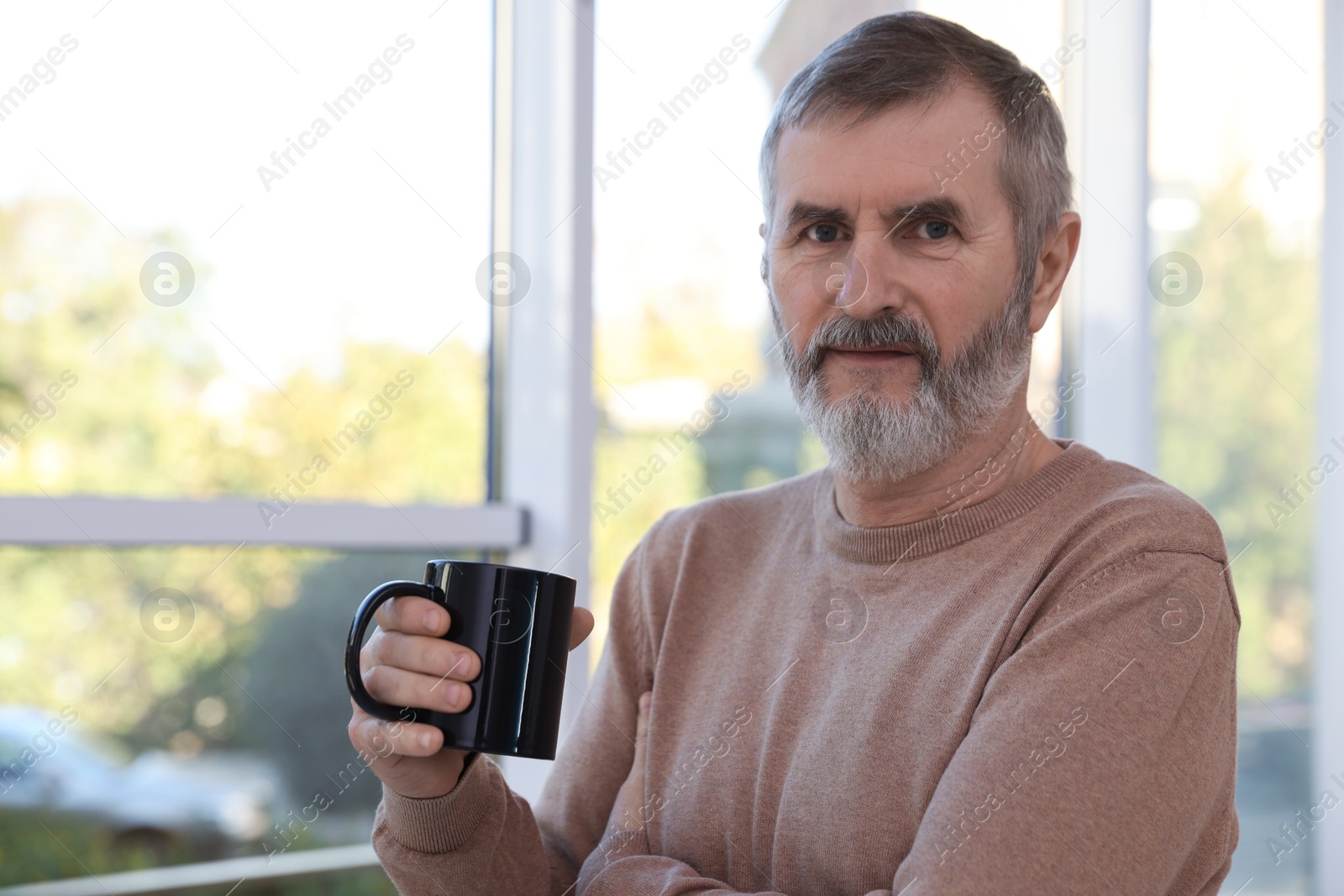 Photo of Mature man with cup of hot drink at home. Space for text