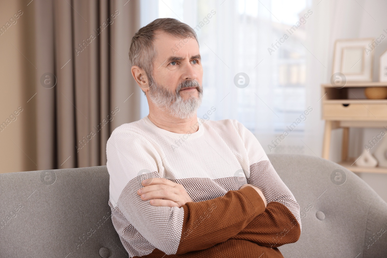 Photo of Mature man with crossed arms on sofa at home