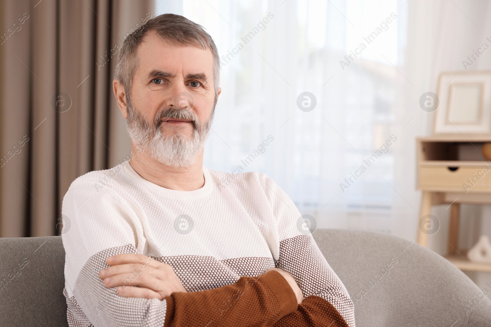 Photo of Mature man with crossed arms on sofa at home. Space for text