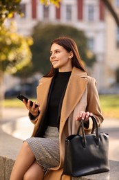 Smiling businesswoman in stylish suit with smartphone outdoors