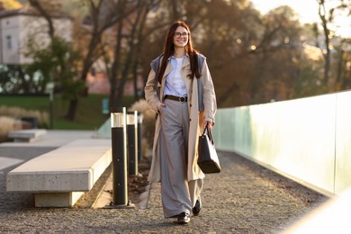 Smiling businesswoman in stylish suit walking outdoors at morning