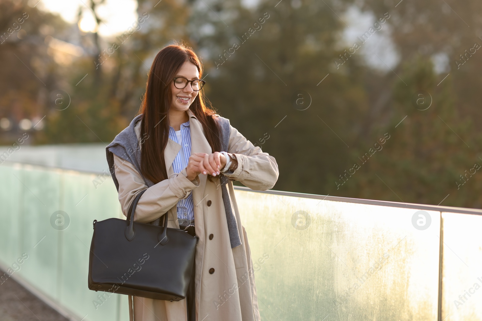 Photo of Smiling businesswoman in stylish suit looking at wristwatch outdoors