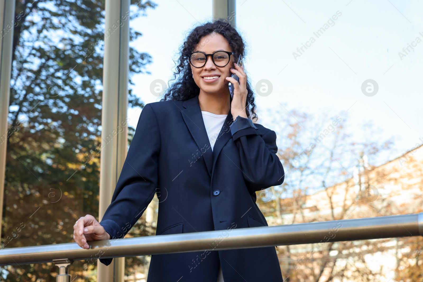 Photo of Portrait of young woman in stylish suit talking on phone outdoors