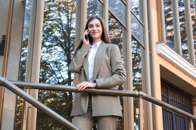 Photo of Portrait of young woman in stylish suit talking on phone outdoors, low angle view