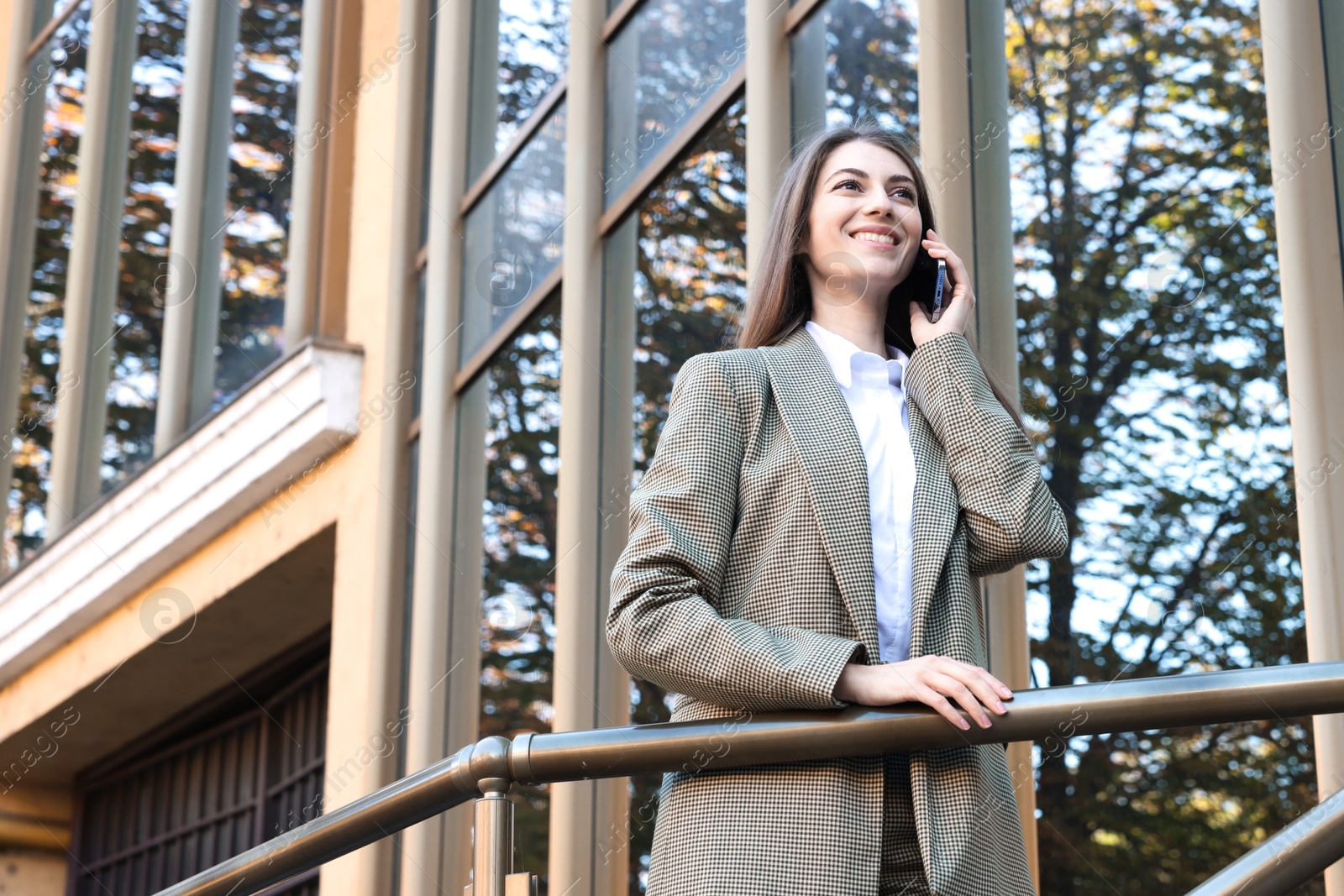 Photo of Portrait of young woman in stylish suit talking on phone outdoors, low angle view