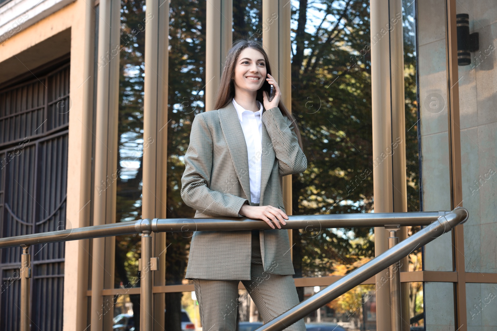 Photo of Portrait of young woman in stylish suit talking on phone outdoors