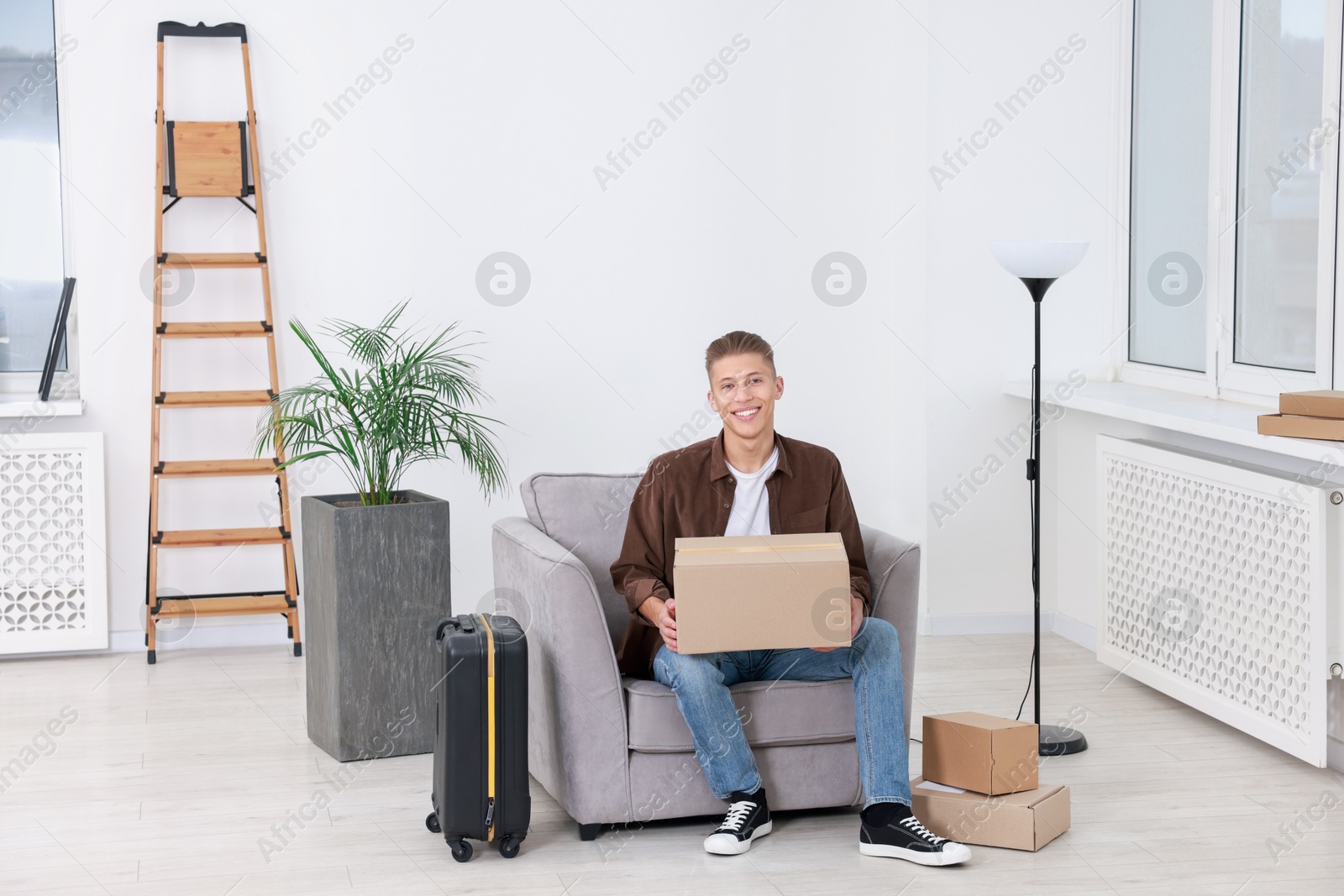 Photo of Happy man with moving boxes and suitcase in new apartment. Housewarming party