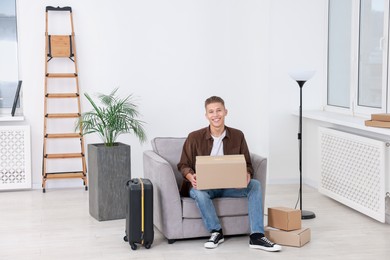 Photo of Happy man with moving boxes and suitcase in new apartment. Housewarming party