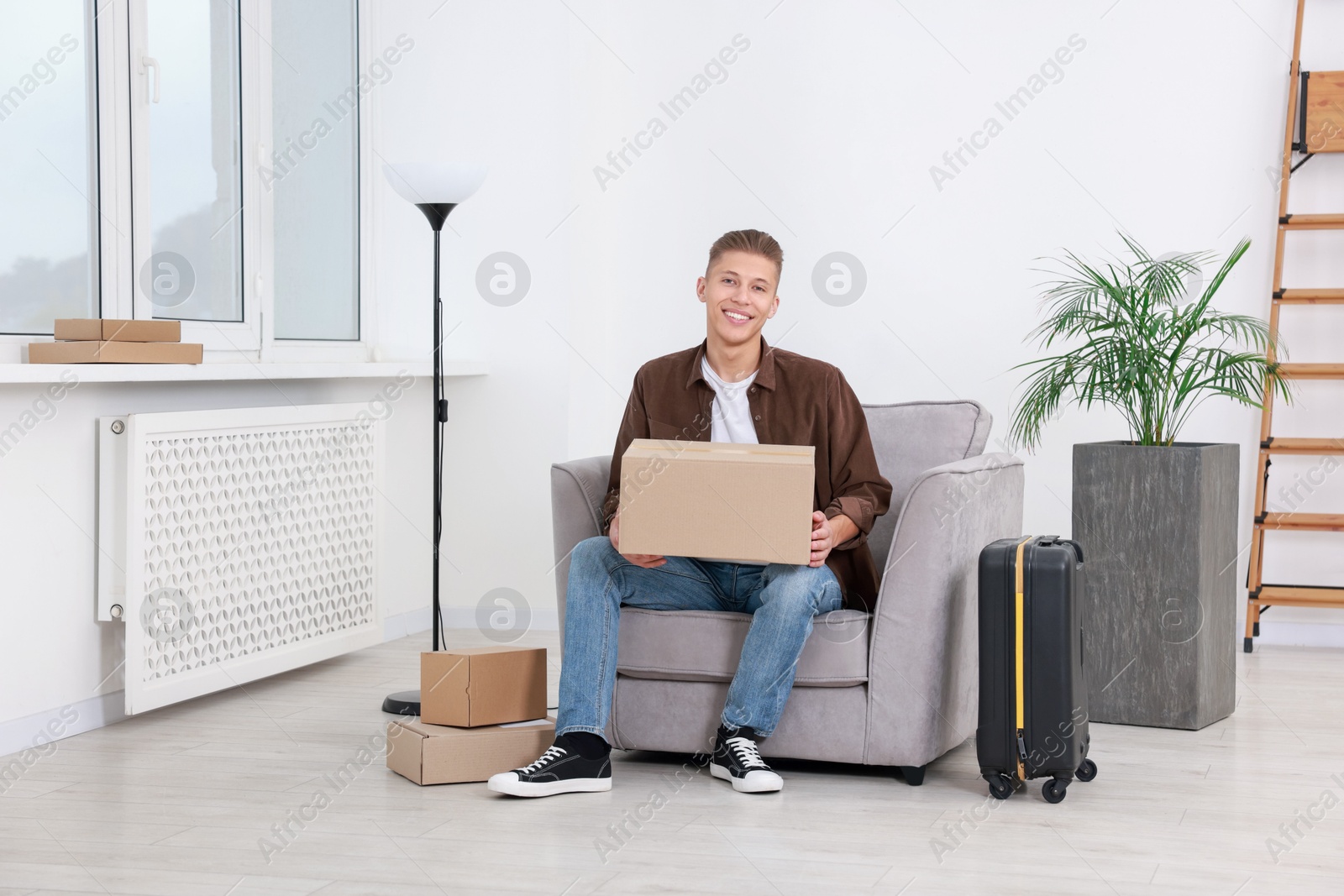 Photo of Happy man with moving boxes and suitcase in new apartment. Housewarming party