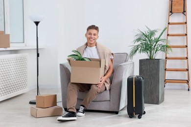 Photo of Happy man with moving boxes and suitcase in new apartment. Housewarming party