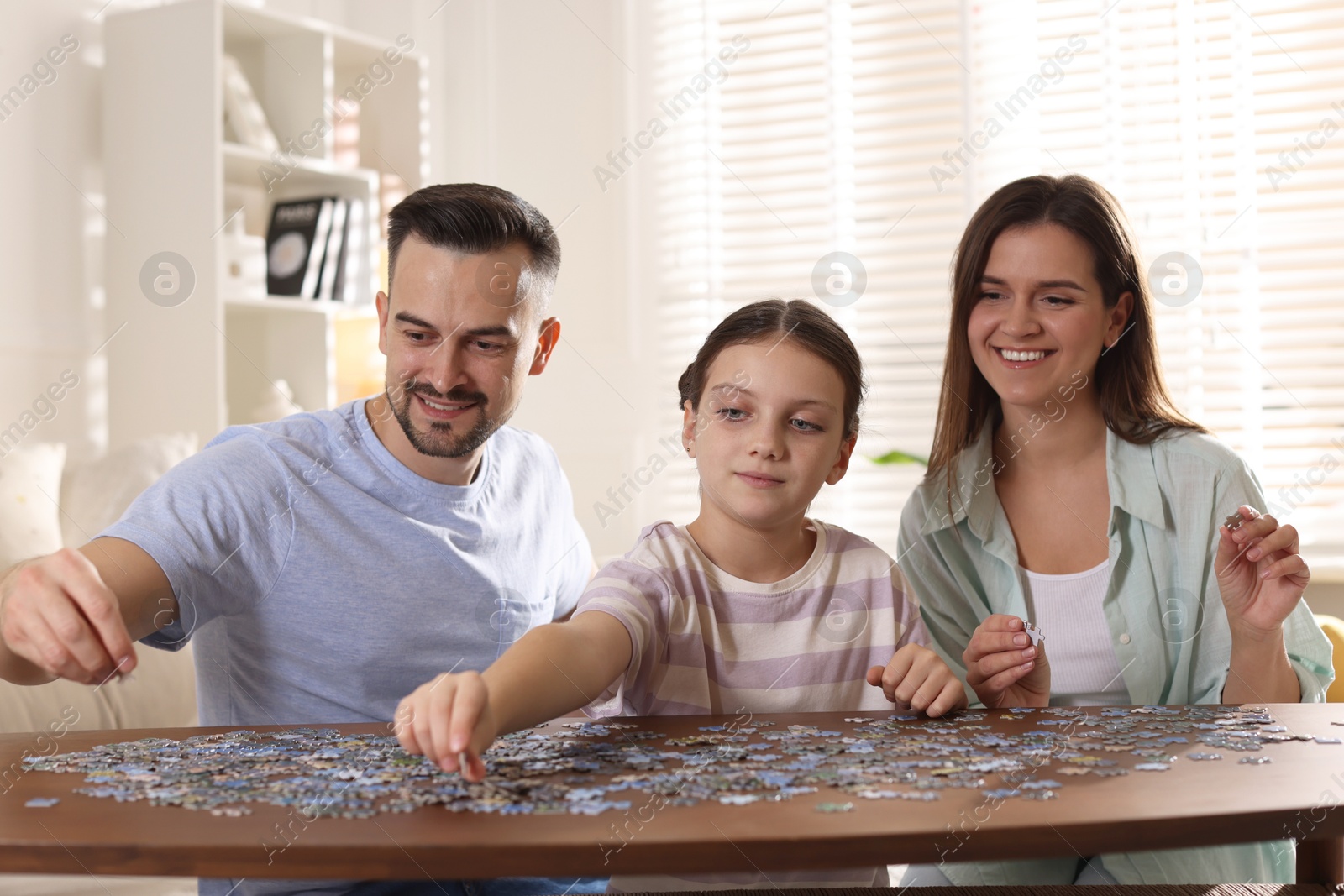 Photo of Happy parents and their daughter solving puzzle together at wooden table indoors