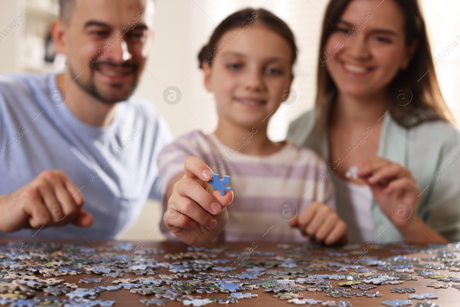 Photo of Happy parents and their daughter solving puzzle together at wooden table indoors, selective focus