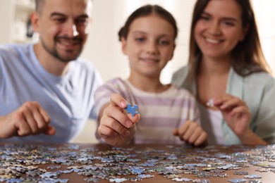 Happy parents and their daughter solving puzzle together at wooden table indoors, selective focus