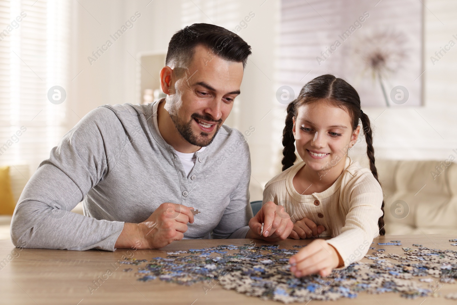 Photo of Happy father and his daughter solving puzzle together at wooden table indoors