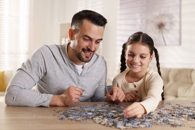 Happy father and his daughter solving puzzle together at wooden table indoors