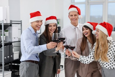 Photo of Happy coworkers clinking glasses of wine during office Christmas party