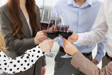 Photo of Happy coworkers clinking glasses of wine during office Christmas party, closeup