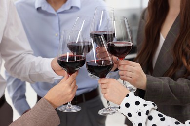 Photo of Happy coworkers clinking glasses of wine during office Christmas party, closeup