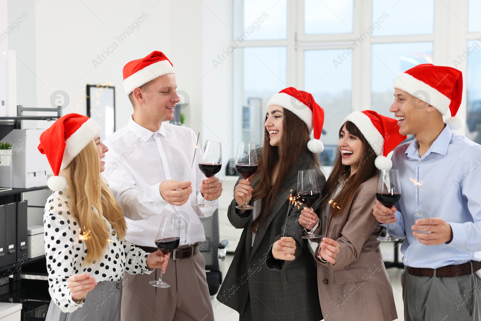 Photo of Happy colleagues with sparklers and glasses of wine at Christmas party in office