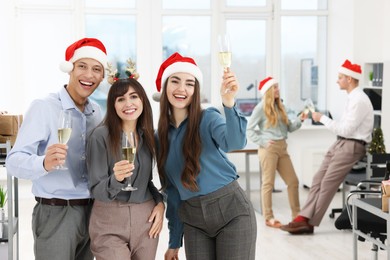 Photo of Cheerful coworkers in Santa hats with glasses of wine at office Christmas party