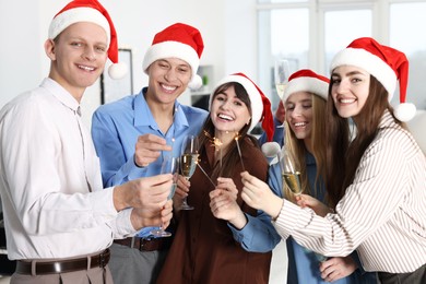 Photo of Happy colleagues with sparklers and glasses of wine at Christmas party in office