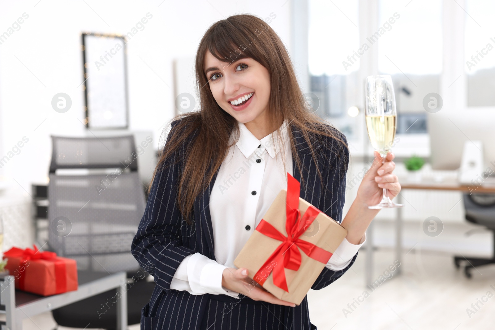 Photo of Happy woman with gift and glass of wine at office Christmas party