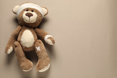 Photo of Teddy bear with bandages and sticking plasters on beige background, top view. Space for text