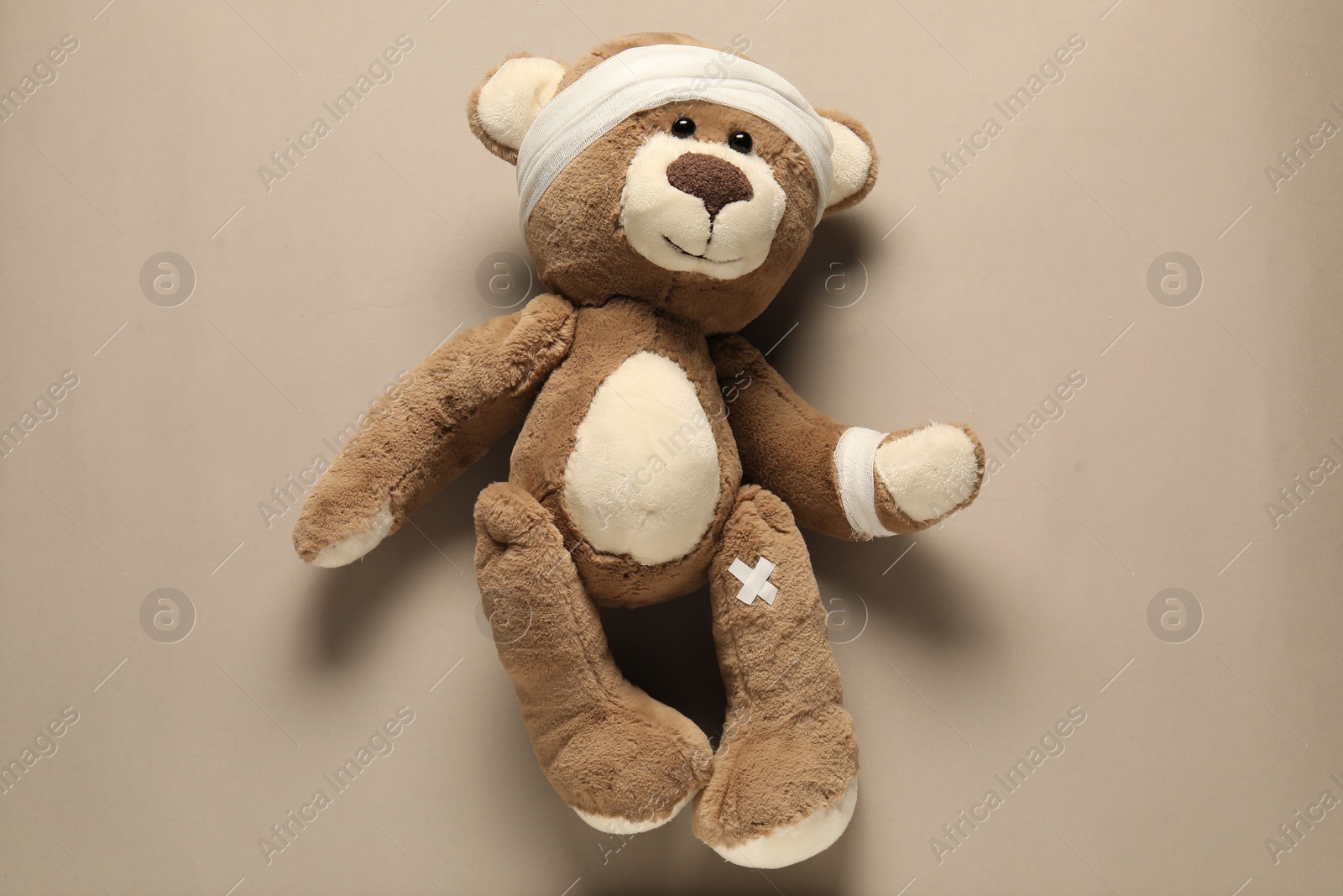 Photo of Teddy bear with bandages and sticking plasters on beige background, top view