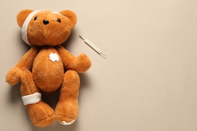 Photo of Teddy bear with bandages, thermometer and sticking plasters on beige background, top view. Space for text