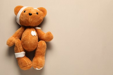 Photo of Teddy bear with bandages, thermometer and sticking plasters on beige background, top view. Space for text