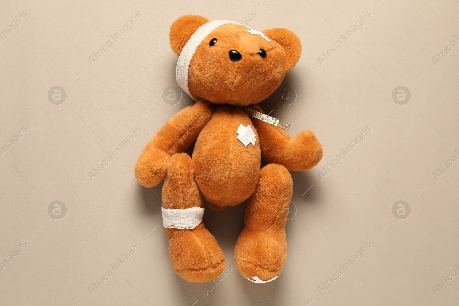 Photo of Teddy bear with bandages, thermometer and sticking plasters on beige background, top view