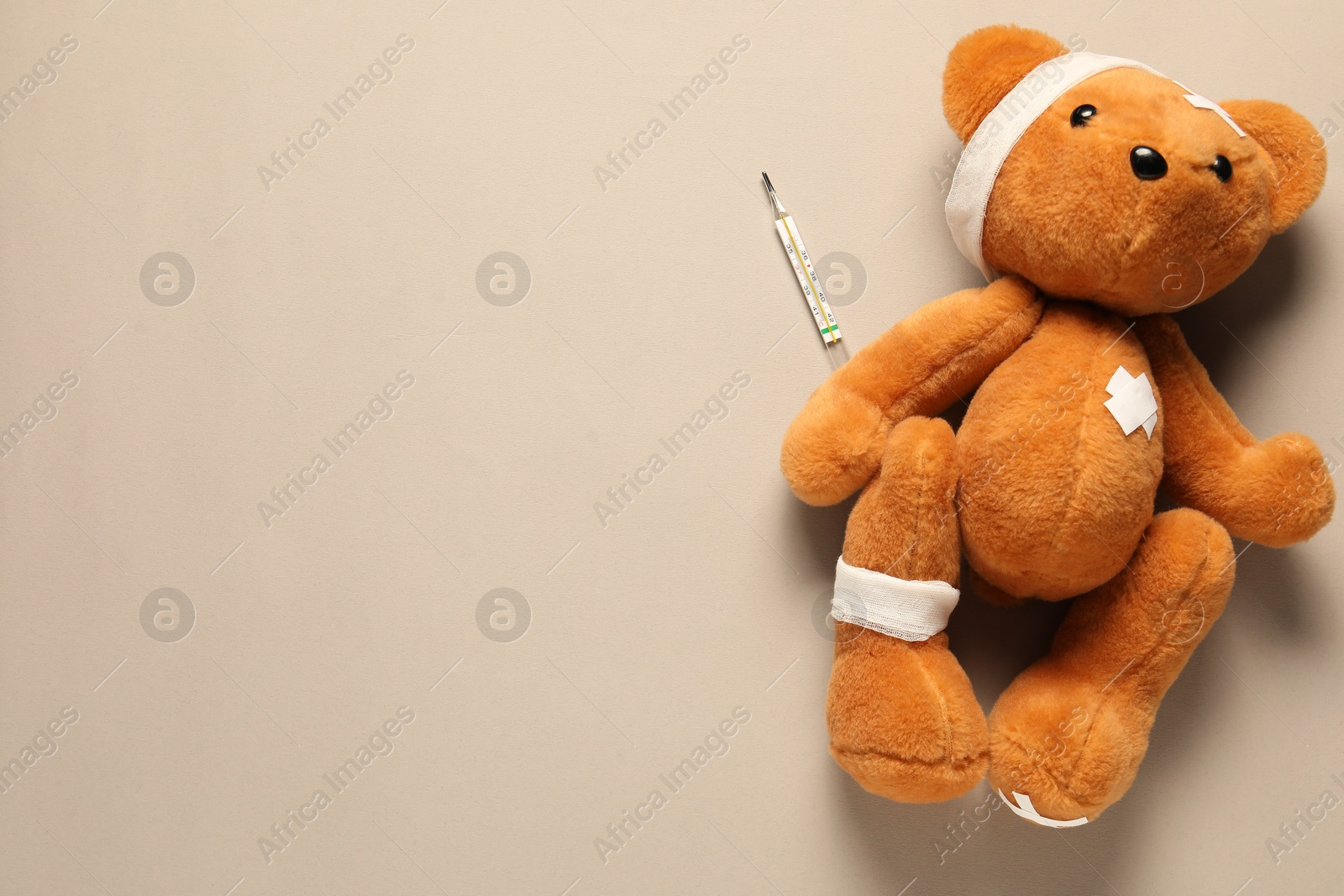 Photo of Teddy bear with bandages, thermometer and sticking plasters on beige background, top view. Space for text