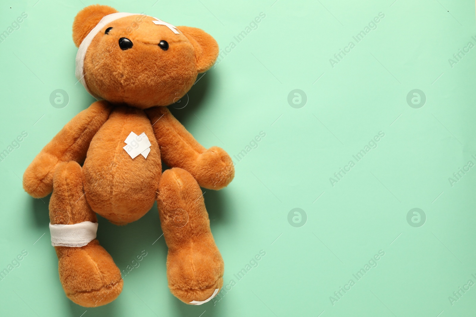 Photo of Teddy bear with bandages and sticking plasters on turquoise background, top view. Space for text