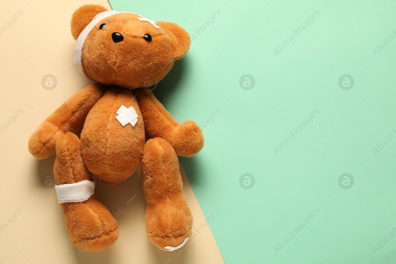 Photo of Teddy bear with bandages and sticking plasters on color background, top view